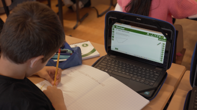 Leerling werkt met een schrift naast een laptop